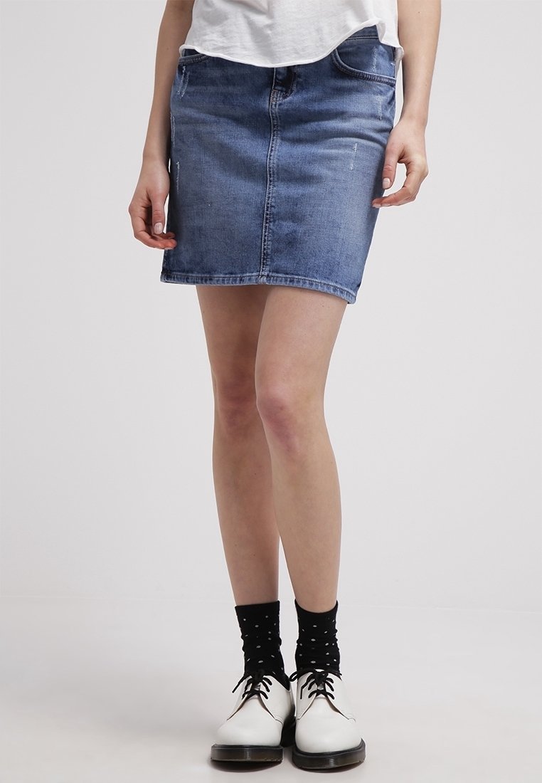 Jeansminikjol i medelblåtvätt, med en åtsittande silhuett, framfickor och en ren fåll, i kombination med vita skor och prickiga strumpor.