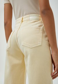 Hoch geschnittene, hellgelbe Jeanshose mit zwei Gesäßtaschen und feinen Nähten. Mit Markenlabel am Bund.