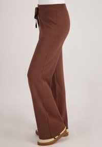 Bruine, hooggetailleerde, wijde broek met trekkoord in de taille en een gladde, zachte textuur. Details van het designsplits aan de zijkant zichtbaar.