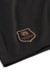 Svart atletisk tyg med en текстurerad yta. Har en rosa-guld sköldlogotyp med texten "STADÉ RENNAIS FOOTBALL CLUB" och etableringsår 1901.