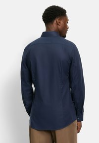 Nachtblaues Langarmhemd aus strukturiertem Stoff, mit Knopfleiste und klassischer Passform. Verfügt über Manschetten mit zwei Knöpfen und einem dezenten Muster.