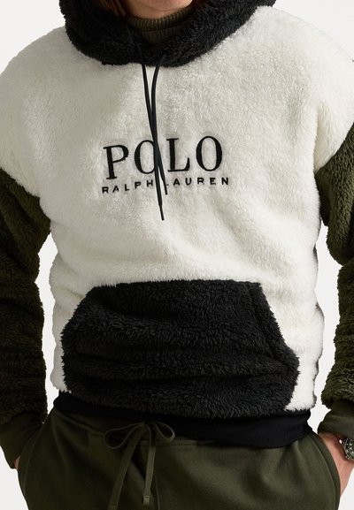 Sweat à capuche en polaire blanc et gris foncé avec un logo noir, poche avant et capuche réglable avec cordon. Tissu texturé avec des manches contrastantes.