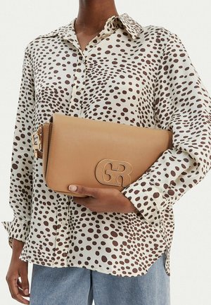 Persona con una camisa blanca con lunares marrones sosteniendo un bolso de mano de cuero marrón claro con las iniciales entrelazadas doradas "GR".