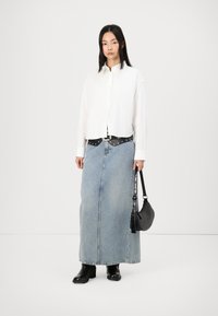 Bílá košile na knoflíky, černý páskový akcent, modrá denimová maxi sukně, černé boty na podpatku a malá černá kabelka. Jednoduchý design, neformální styl.