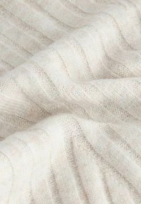 Lys beige strikket stof med ribbet tekstur, der har subtile variationer og et blødt, hyggeligt udseende.
