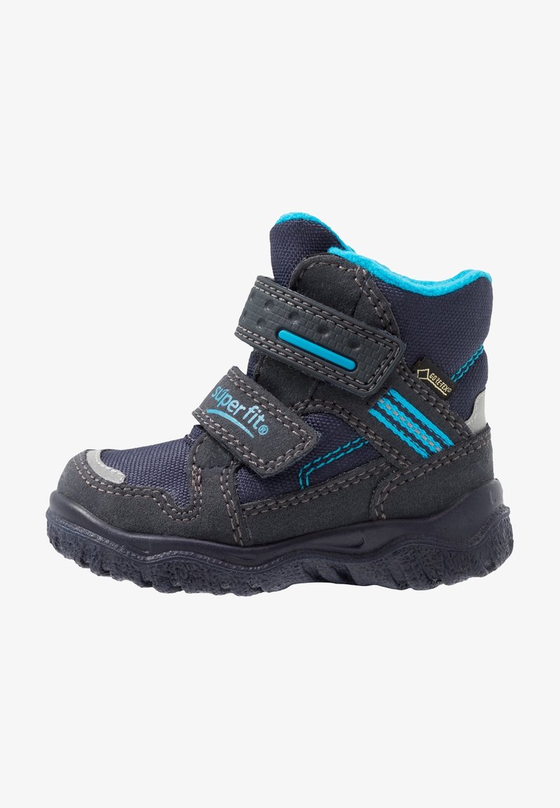 Kinderschuh mit einem Obermaterial aus navy-blauem Textil und grauem Wildleder, türkisfarbenen Akzenten, zwei Klettverschlüssen und einer strukturierten Gummisohle für besseren Halt.