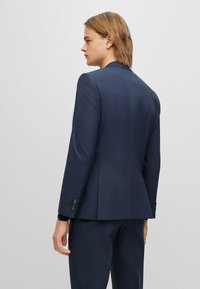 Giacca navy realizzata in tessuto morbido, con un design aderente, spalle strutturate e polsini a quattro bottoni.