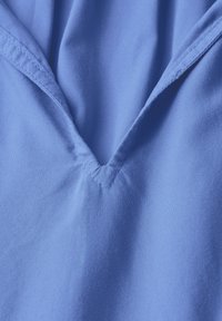 Tessuto blu chiaro con scollatura a V, con una texture liscia e dettagli di cucitura sottili. Il tessuto appare morbido e si drappeggia dolcemente.