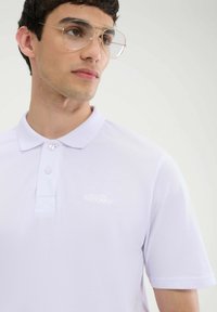 Jasnofioletowa koszulka polo z teksturowanym splotem, z klasycznym kołnierzykiem, dwoma guzikami oraz subtelnym haftowanym logo na piersi.