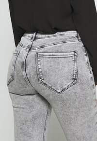 Jeans de mezclilla gris de cintura alta y ajustados, con un lavado desgastado, costuras en contraste y dos bolsillos traseros con bordes reforzados.