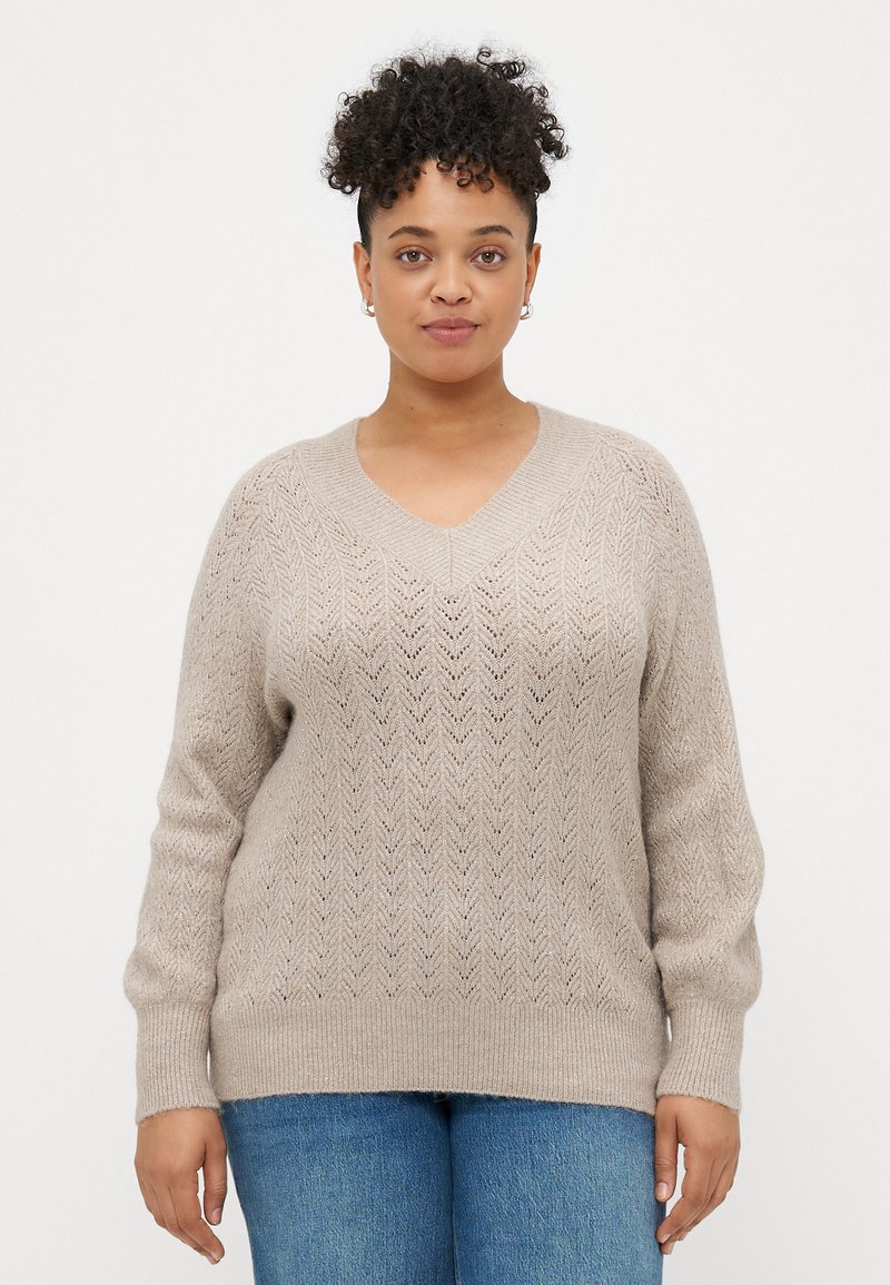 Beige strikket genser med V-hals, med et chevronmønster og ribbestrikkede mansjetter. Myk tekstur, avslappet passform og noe oversized design.