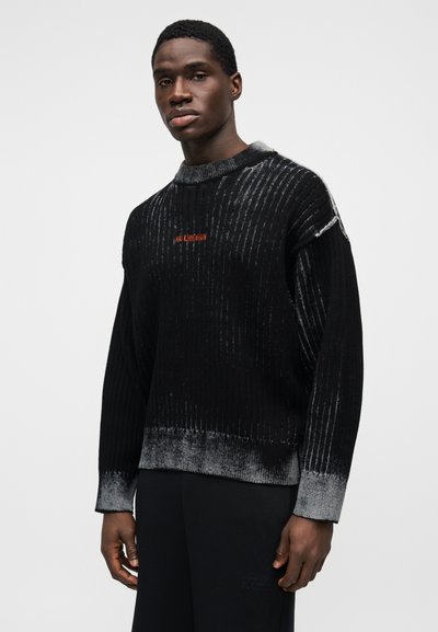 Χοντρό μαύρο πουλόβερ με ριμπ υφή, διαβαθμισμένες γκρι λεπτομέρειες και στρογγυλή λαιμόκοψη. Μικρό κέντημα με κόκκινο λογότυπο στο στήθος.