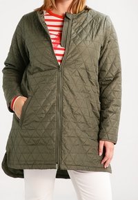 Quilted olive-green coat with a high collar and diagonal stitching. Features zip closure and side pockets, worn over a red and white striped top.