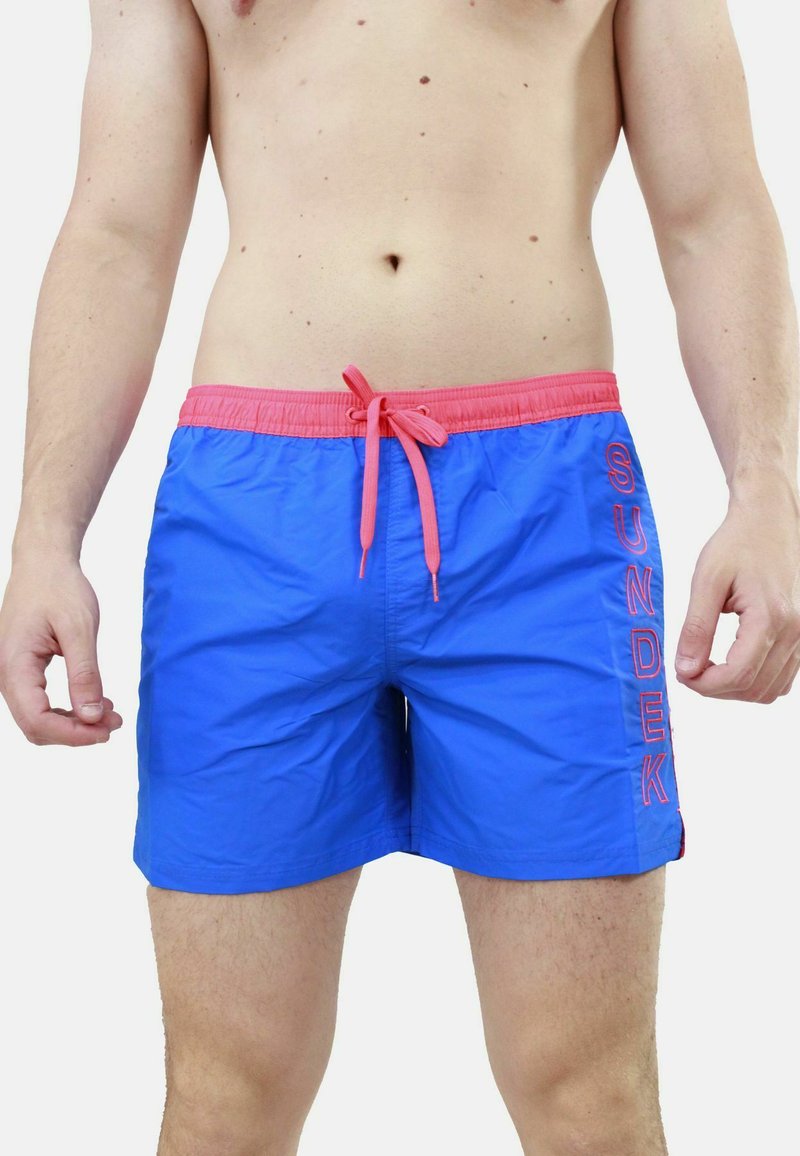 Pantaloni da nuoto blu con vita e cordino rosa. Presentano il logo 'SUNDEK' in rosa sul lato. Realizzati in un materiale leggero e morbido.