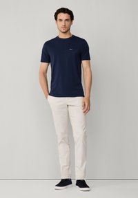 Granatowa koszulka z krótkim rękawem z kieszonką na piersi, zestawiona z jasnobeżowymi spodniami i czarnymi butami, o minimalistycznym wzornictwie.