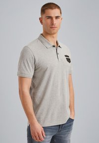 Polo de color gris claro con una textura suave, de manga corta y con tapeta de tres botones. Presenta un pequeño bolsillo negro de acento en el pecho.
