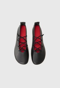 Zwarte leren schoenen met een gladde textuur, met een laag uitgesneden ontwerp en rode binnenzolen, verfraaid met zwarte veters over de bovenkant.