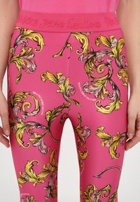 Leggings rosa con un motivo floreale in giallo e rosa. La vita è testurizzata con lettere in rilievo.