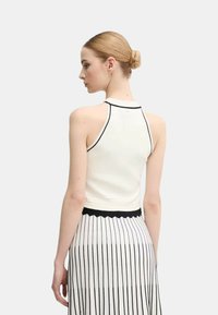 Top bianco senza maniche con bordino nero, caratterizzato da una silhouette aderente. Il retro è semplice con uno scollo basso, abbinato a una gonna a righe bianche e nere.