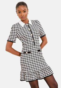 Fekete-fehér mintás kockás rövid ujjú ruha gallérral, gombos záródással és fodros szegéllyel. Aranyszínű gombokkal és fekete szegélydíszítéssel.