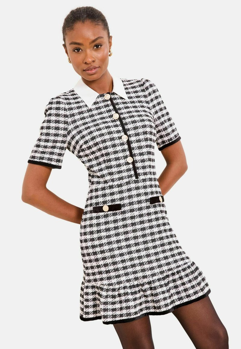 Fekete-fehér mintás kockás rövid ujjú ruha gallérral, gombos záródással és fodros szegéllyel. Aranyszínű gombokkal és fekete szegélydíszítéssel.