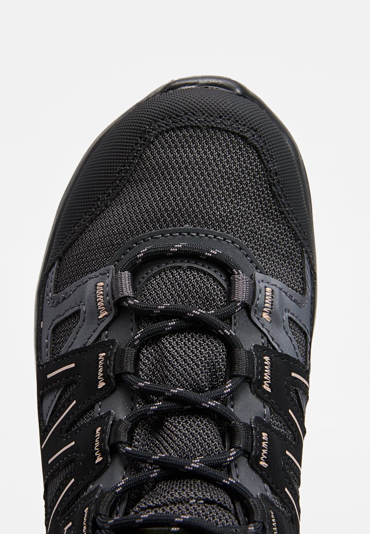Chaussure de sport noire avec tige en mesh, embout renforcé et accents réfléchissants. Elle dispose d'un système de laçage et d'une surface texturée pour une meilleure adhérence.