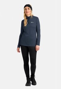 Marineblaues Langarmoberteil mit Reißverschluss am Hals, kombiniert mit schwarzen Leggings. Der Stoff wirkt glatt, das Design ist figurbetont und die Ärmel haben Daumenlöcher.