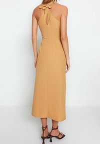 Senapsgul halterneck-klänning med en nyckelhålsdetalj i ryggen, golvlång design, slät textur och figurnära midja.