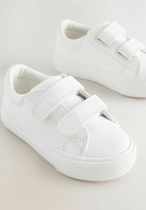 Balti sporta apavi ar gludu sintētisku virsu, noapaļotu purngalu, diviem Velcro siksniņām un gumijas zoli ar teksturētu saķeri.