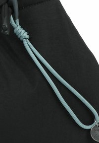 Cordón de color azul claro, atado y encintado en el extremo, unido a una pequeña etiqueta metálica redonda sobre una tela negra.