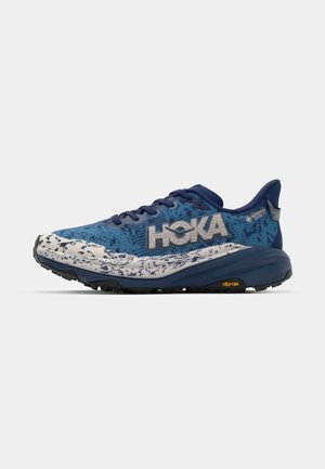 Buty do biegania w terenie z niebiesko-białą cholewką, posiadające fakturowany wzór, sztywną podeszwę i podeszwę Vibram dla lepszej przyczepności.
