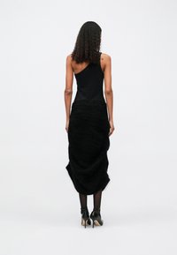 Top preto sem mangas com decote assimétrico, combinado com uma saia preta texturizada, apresentando um design drapeado e saltos pretos até ao tornozelo.