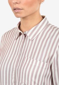 Camicia a righe con bottoni, caratterizzata da righe alternate di rosa chiaro e bianco, colletto a punta e taschino sul petto. Finitura in tessuto testurizzato.