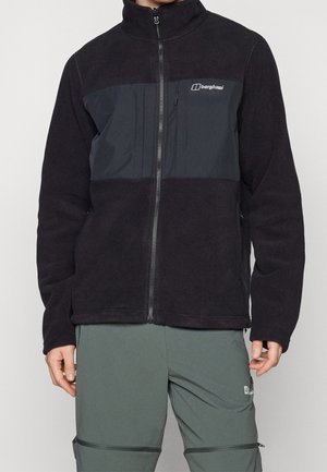 Chaqueta de forro polar negra con un panel frontal gris, cierre de cremallera, cuello alto y logotipo en el pecho. Textura suave, diseño ajustado y mangas largas.