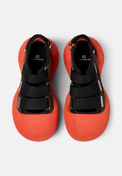 Paire de sandales noires avec des semelles en mousse rouge épaisse et trois brides noires réglables, avec l'inscription CamperLab à l'intérieur.