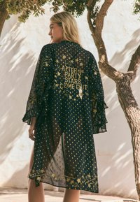 Juodas permatomas kimono su auksinėmis žvaigždėmis ir taškeliais, raukiniais rankovėmis ir užrašu "PO ŠVENTĖS PASIRODO ŽVAIGŽDĖS" ant nugaros.