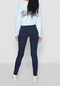 Sudadera corta azul claro con "TOMMY HILFIGER" impreso en la espalda, combinada con jeans ajustados azul marino oscuro y zapatillas blancas.