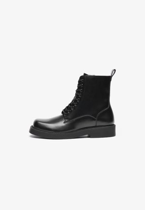 Schwarze Lederstiefeletten mit glatter Oberfläche, rechteckiger Zehenpartie, Schnürdesign und flacher Gummisohle. Enthält eine Zuglasche hinten.