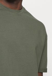 Olivenfarvet kortærmet T-shirt lavet af blød bomuld, med rund halsudskæring og omviklede ærmer, med en glat og let struktureret overflade.