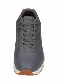 Zapatilla de cuero gris con diseño perforado, punta redonda, cordones grises y suela de goma. Presenta la marca "SKECHERS" en el lateral.