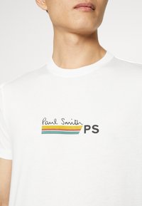 Bílý bavlněný tričko s černým a barevným pruhovaným logem se textem "Paul Smith" a "PS". Krátké rukávy a design s kulatým výstřihem.