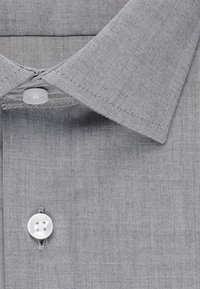 Camicia di lino grigia che mostra un primo piano di un bottone e del colletto. Il tessuto ha una sottile trama, con un singolo bottone rotondo bianco allacciato.