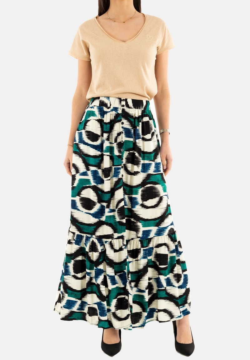 T-shirt beige a scollo a V abbinato a una lunga gonna a strati con un audace motivo astratto verde, blu e nero su uno sfondo bianco.