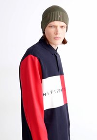 Polo shirt in navy, red, and white with a color-block design. Features a collar and a logo. Accompanied by a ribbed green beanie.