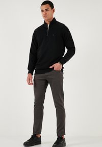 Melnā zip-aizdare džempera ar garām piedurknēm, apvienots ar pelēkiem šauriem biksēm un melniem sporta apaviem; gluda tekstūra, ikdienišķa piegriezuma, minimāla logotipa detaļa.