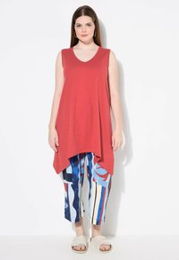 Top smanicato rosso con scollo a V e design fluido, abbinato a pantaloni cropped a righe blu e bianchi, comodi e larghi. Sandali chiari.