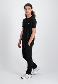 Sort t-shirt med korte ærmer og et lille logo på brystet, parret med sorte sweatpants med et subtilt tekstmønster, båret med hvide træningssko.