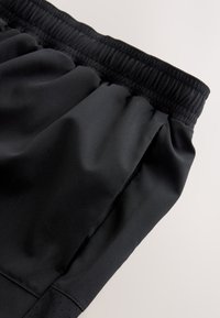 Gros plan de la ceinture élastique noire et de la poche latérale sur un pantalon ou un short en tissu lisse.