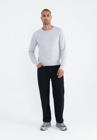 Ljust grått våffelmönstrat tröja, svarta byxor och silverfärgade sneakers, stående mot en vit bakgrund. Släta texturer och avslappnad passform.
