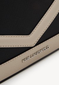 Černá textilní taška s béžovými akcenty, která má design s chevron vzorem, texturovaný povrch a stříbrné logo "KARL LAGERFELD".